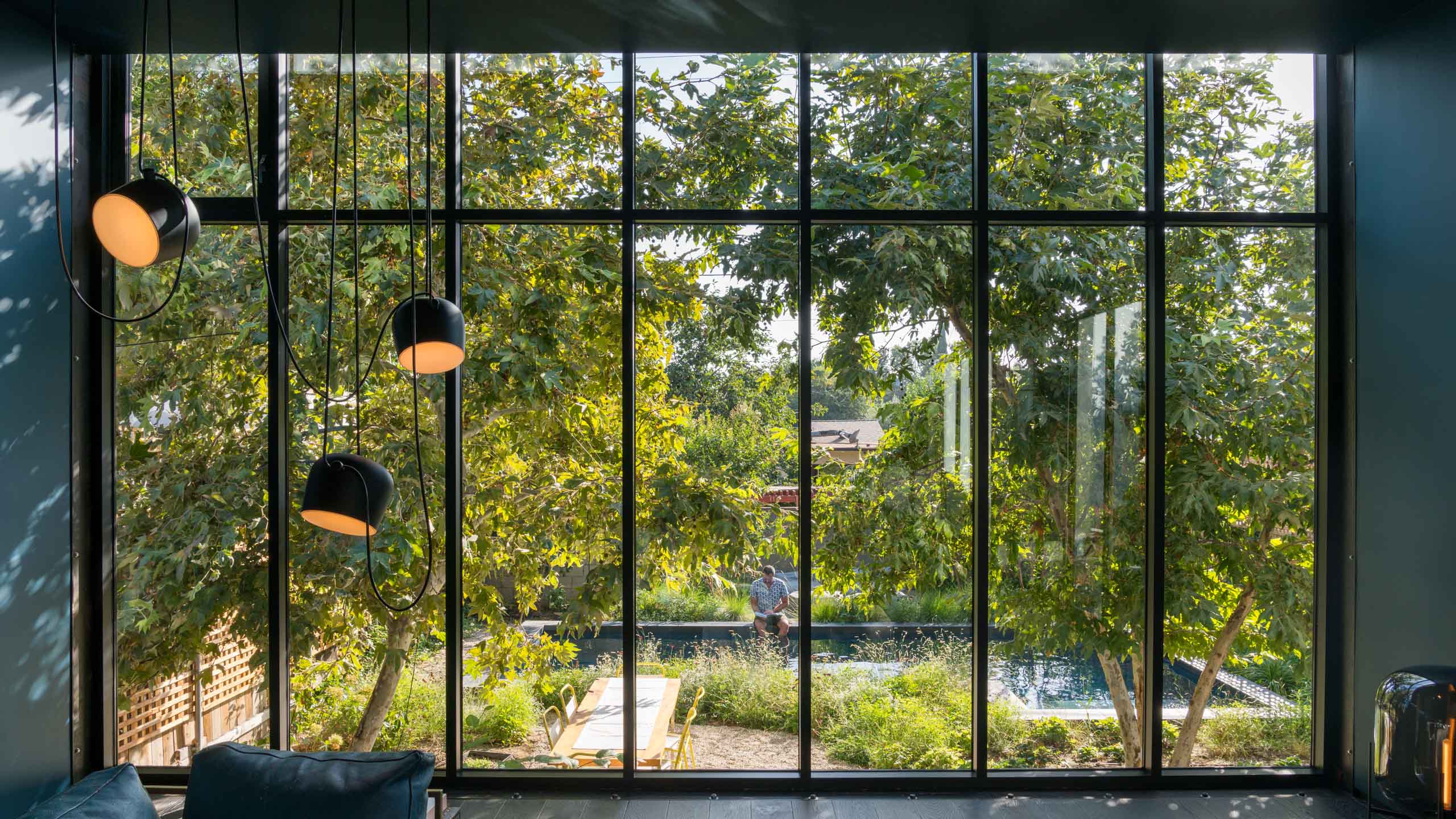 Interior living room looking to the lush green backyard through floor to ceiling windows