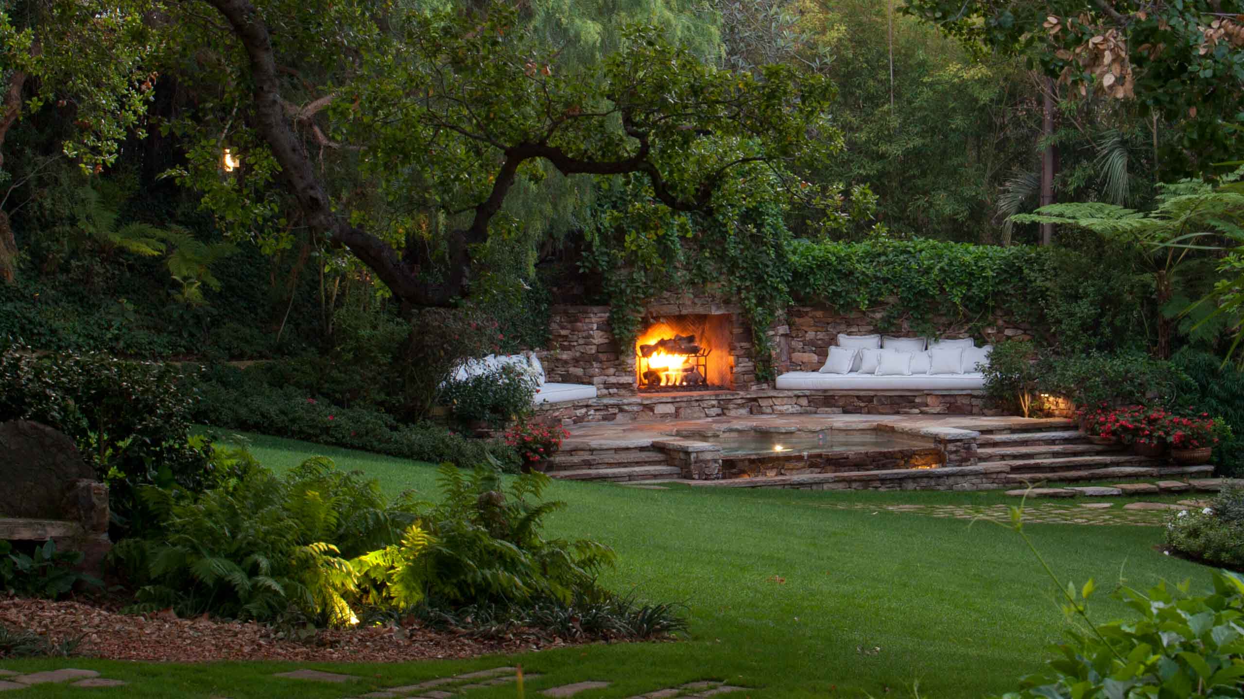 Landscape with lush and green trees and plants adjacent to cozy lounge furniture and a fire place